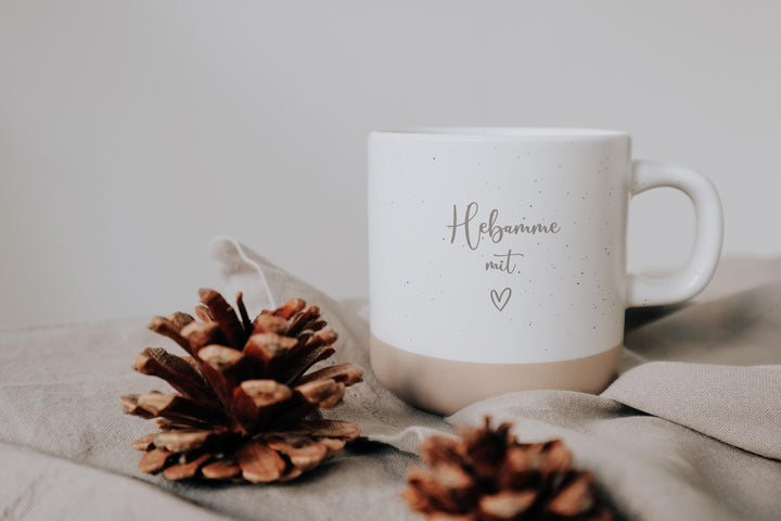 Steingut Tasse mit dickem Henkel als Geschenk und zum Danke sagen an die Hebammen.  Tasse mit weißer matter Lasur und kleinen sprenkeln der Oberfläche und unglasiertem Bodendesign in Natur, Graviert mit Hebamme mit Herz.