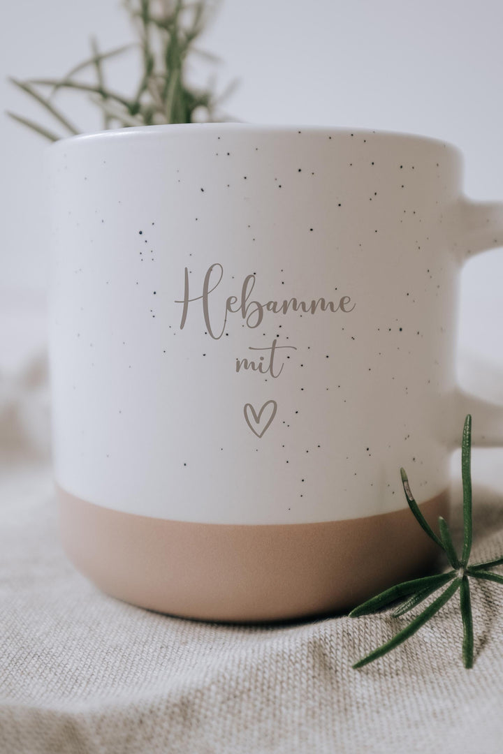 Steingut Tasse mit dickem Henkel als Geschenk und zum Danke sagen an die Hebammen.  Tasse mit weißer matter Lasur und kleinen sprenkeln der Oberfläche und unglasiertem Bodendesign in Natur, Graviert mit Hebamme mit Herz.
