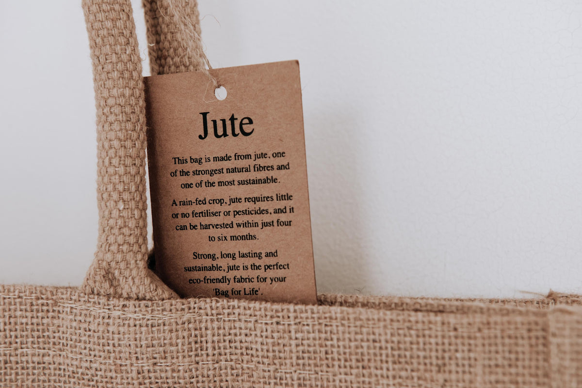 Nahaufnahme eines Etiketts, das die Nachhaltigkeit der Jutetasche hervorhebt. Das Etikett erklärt, dass Jute eine der stärksten und umweltfreundlichsten Naturfasern ist, die schnell wächst und ohne Pestizide angebaut werden kann.